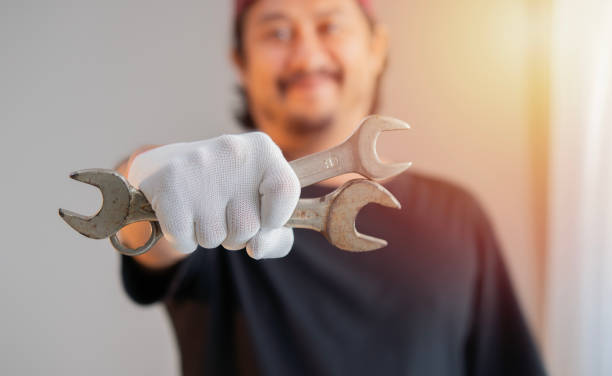 Mechanic posing with a wrench in his hand and gesturing thumbs up at repair shop.