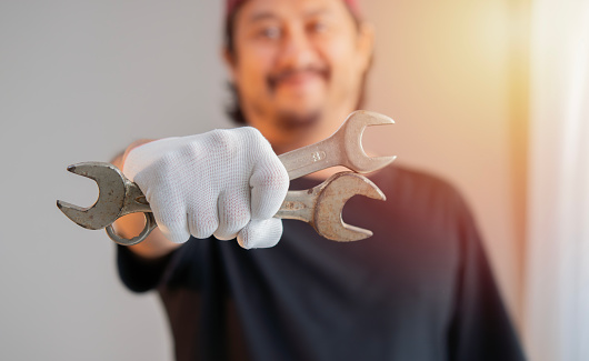 Man's hand wearing white cloth gloves and holds a spanners over on sunlight background. Close up.