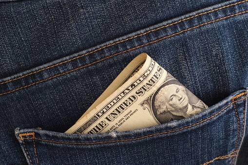 A close-up shot of a one dollar banknote in the back pocket of blue jeans. Close up.