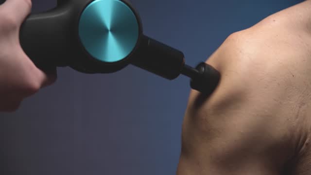 Percussion massage of the shoulder of a male athlete with a shock wave massager. Close-up slow motion. Wave Vibration of the body from the massager