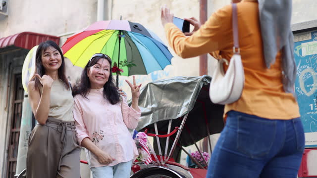 Diverse female travellers take photos together using a smartphone while enjoying a ride on a trishaw through the historic old town of Georgetown, Penang