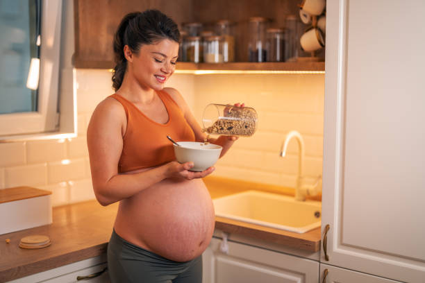 istock A happy pregnant woman pouring cereal in a bowl while standing in a kitchen 2149077652