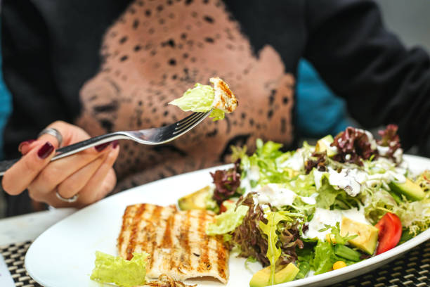 A woman sits at a table, eating a salad with a fork.