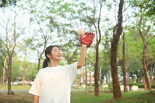 Cheerful asian girl in leather baseball glove catching ball. Sport, activity and people concept.