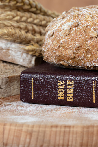 Holy bible book and loaf of bread with wheat on wooden table. Close-up. Word of God Jesus Christ as spiritual food for Christians, biblical concept.