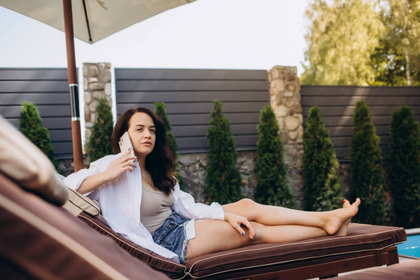 istock Smiling lady lying on deckchair, having call and drinking cocktail on a beach 2149080603