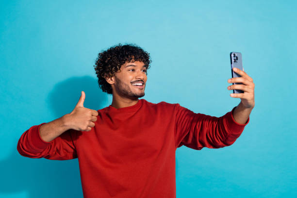 istock Photo of young guy arabian student making selfie with thumb up gesture like symbol using smartphone isolated on aquamarine color background 2149080963