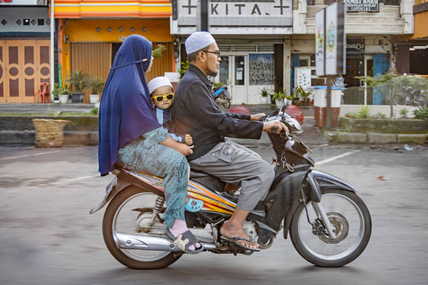 Berastagi, North Sumatra, Indonesia - January 28th 2024:  Islamic family with one kid with funny sunglasses on a motorcycle