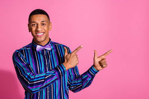 Photo of cheerful positive guy dressed striped shirt showing two fingers empty space isolated pink color background.