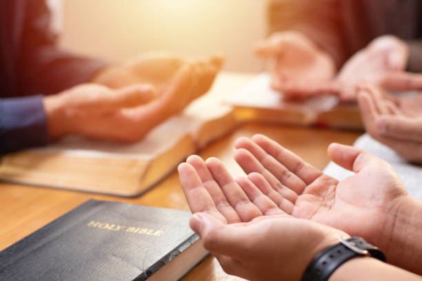 istock Power of hope or love, christian devotion background, bible study group concept. A group of people are gathered around a table with their hands outstretched in prayer over a Holy Bible. 2149082597