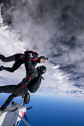 Freefall jumpers jump out of plane together above clouds and snowcapped mountains