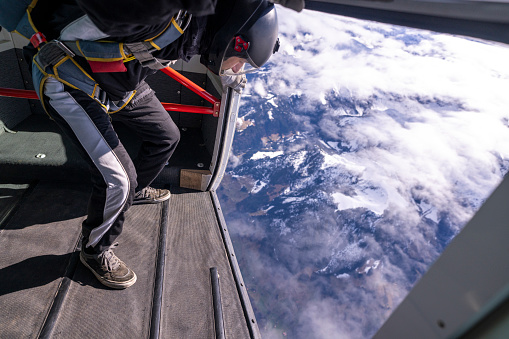 Freefall jumper prepares to jump out of plane above snowcapped Swiss mountain landscape