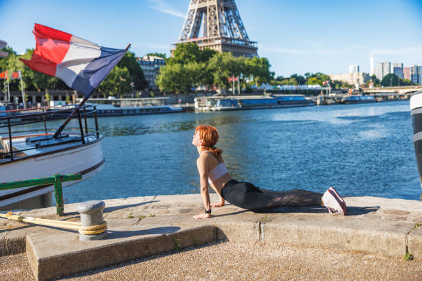 Middle aged woman taking up outdoor exercise, stretching on pier looking at Eiffel Tower in Paris