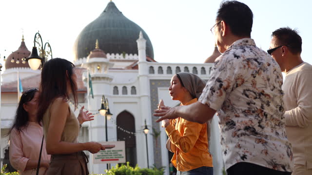 A cheerful Malay local tour guide is explaining the history of the popular mosque to a group of senior Asian tourists while they explore the beautiful historical city of Georgetown, Penang.