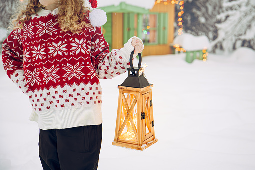 Close up view of child hand holding wood lantern and wearing traditional pattern  Christmas sweater outdoors in snowy winter.