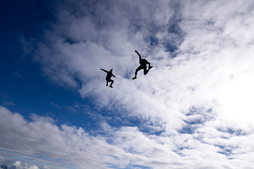 Freefall jumpers face each other mid-air lofty clouds
