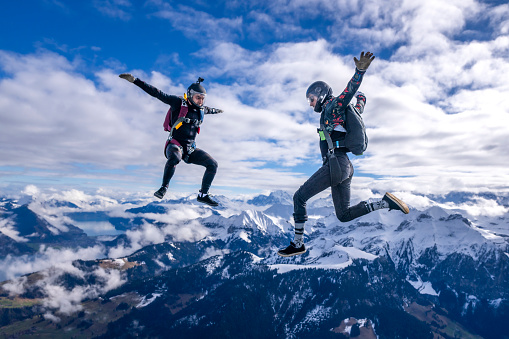 Freefall jumpers face each other mid-air above snowcapped mountains and clouds