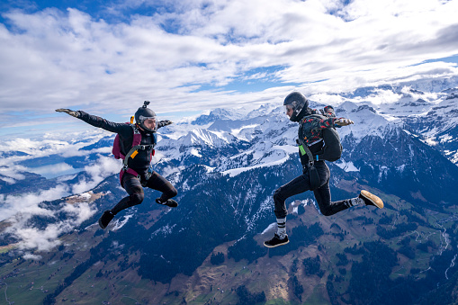 Freefall jumpers face each other mid-air above snowcapped mountains and clouds