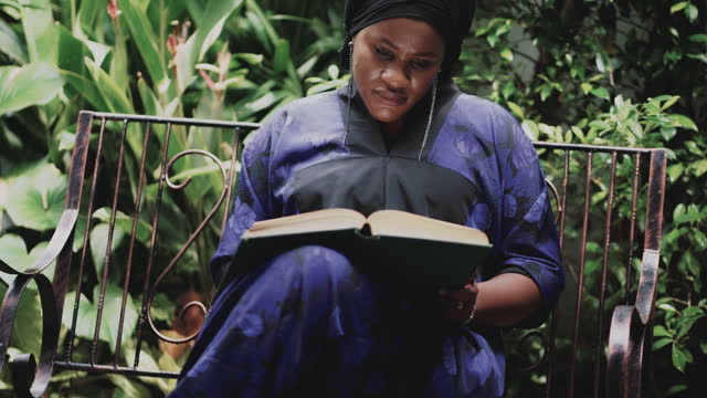 African muslim woman reading a book in courtyard