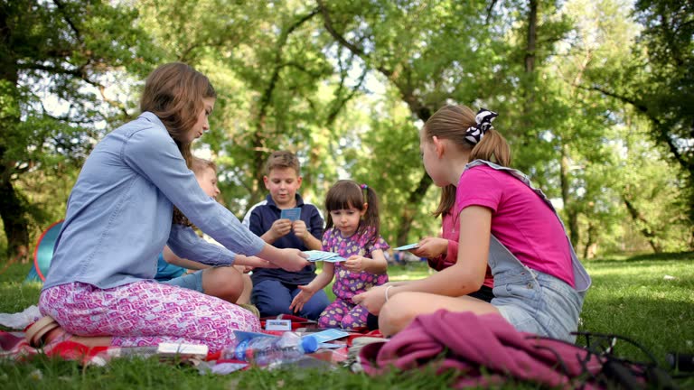 Group of Caucasian boys and girls, using picnic to learn via flash cards