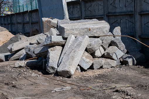 A pile of large and heavy damaged concrete blocks near a reinforced concrete fence at a construction site