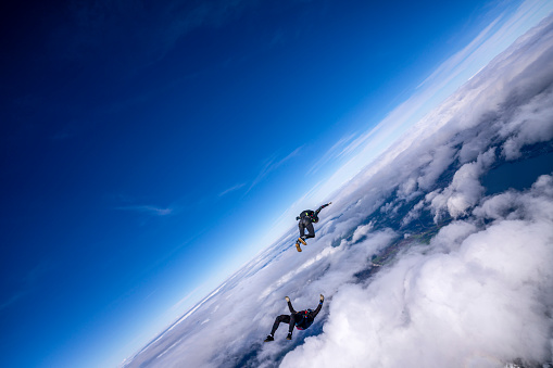 Freefall jumpers upside-down mid-air above clouds and snowcapped Swiss Alps
