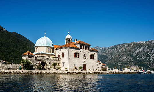 Saint George island in Montenegro, closeup view from Kotor bay in sunny day. Ancient Mediterranean architecture surrounded with mountains in Adriatic sea