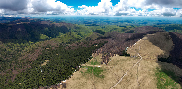 Aerial drone view above Parang Mountains. Springtime, snow still covers the pastures. Clouds are taking over the sky. The beech forest is partially blooming. Carpathia, Romania. Alpine landscape.