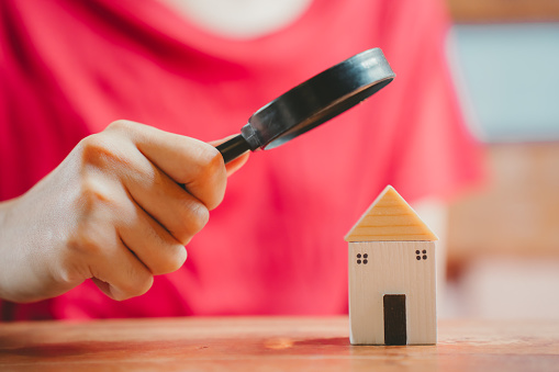 A hand holding a magnifying glass over a miniature house.