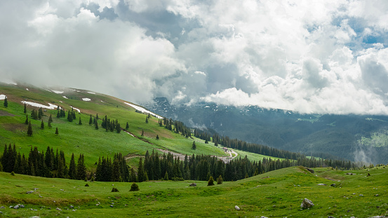Stormy clouds above the mountain peaks in early summer. The sky is clouded but some sunlight passes, reaching the alpine pastures and the spruce woodlands underneath. Carpathia, Romania.