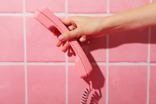 Young curly-haired woman shows astonishment during a phone call, with a vivid pink backdrop enhancing her expressive facial reaction