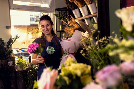 Young woman working in her flower shop holding bouquet.