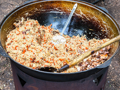 Appetizing traditional Uzbek pilaf in a large cauldron outdoors