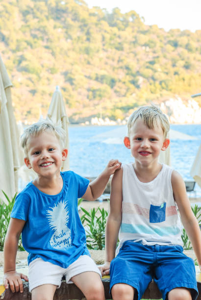 istock Two little boys are sitting on a bench near a beach laughing and engaging playfully 2149092664