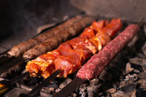 Close-up of an appetizing kebab or shashlik made of fresh meat and lula kebab is cooked on a charcoal grill with smoke.