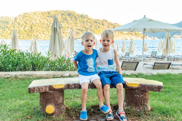 istock Two little boys are sitting on a bench near a beach laughing and engaging playfully 2149092952