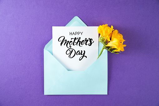 Flowers with blue envelope and greeting card on purple background