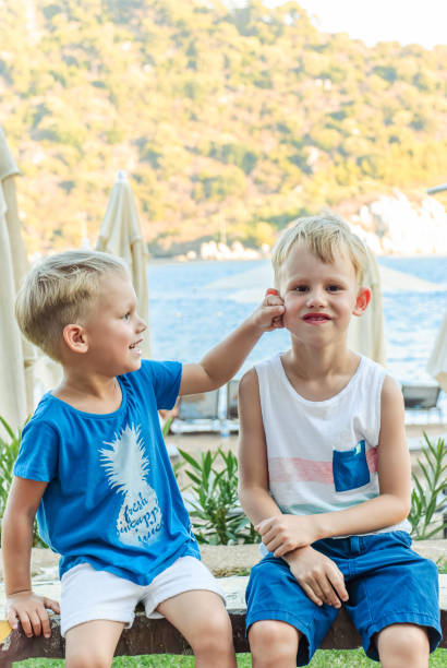 istock Two little boys are sitting on a bench near a beach laughing and engaging playfully 2149093171