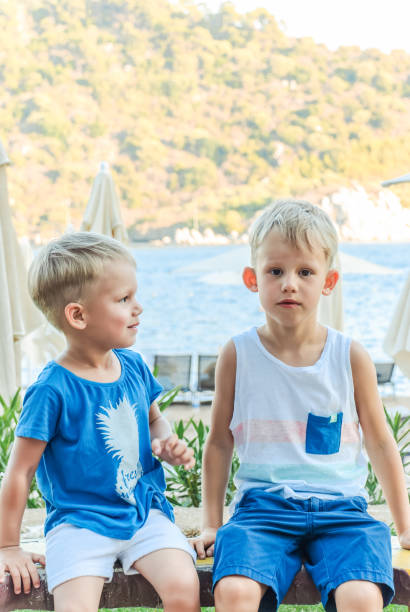 istock Two little boys are sitting on a bench near a beach laughing and engaging playfully 2149093399