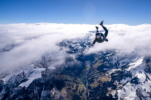 Freefall jumper performs moves mid-air above snowcapped mountains and clouds
