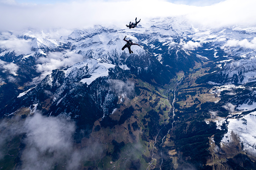Freefall jumpers face to face in mid-air above clouds and snowcapped Swiss Alps