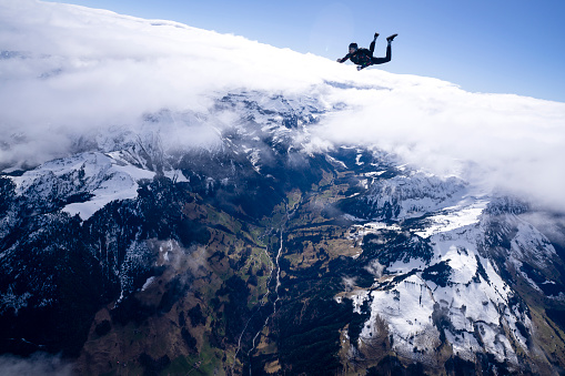 Freefall jumper performs moves mid-air above snowcapped mountains and clouds