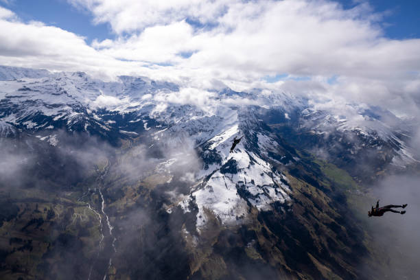 Freefall jumpers face each other mid-air above snowcapped mountains and clouds