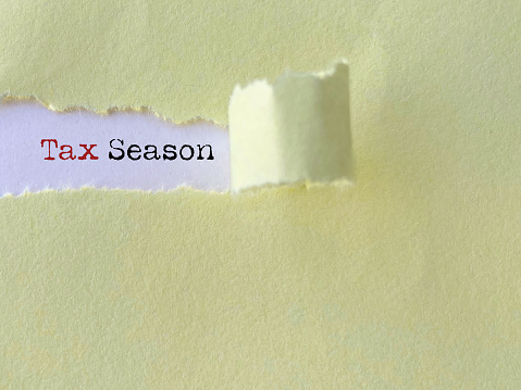 Tax season text behind torn paper background. Stock photo.