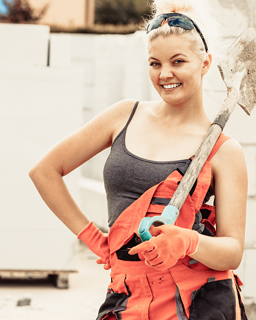 Happy woman worker using shovel standing on industrial construction site, working hard.