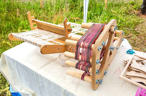 Handmade wooden loom with red and white wools outdoors in summer