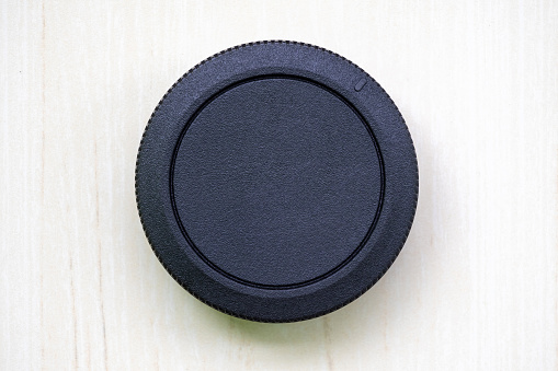 Camera lens cover or lens dust cap without logo on wooden textured white background. A lens cover or lens cap protects camera lenses from scratches, dust, rain, snow, and minor collisions.