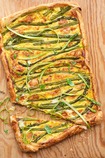 Asparagus pie or tart with eggs, cheese and aromatic herbs, spring Easter recipes. French healthy cuisine, Provencal herbs, azure background. Spring asparagus