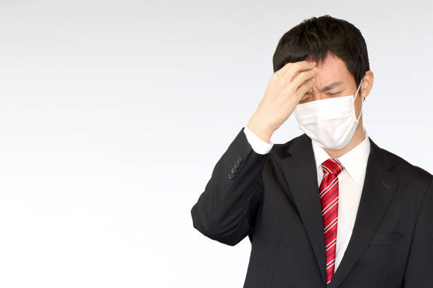 An Asian businessman wearing a suit and mask with a sad expression.