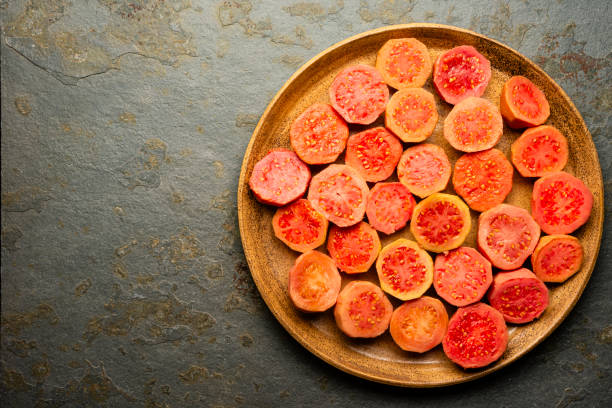 High angle view large group of fresh sweet guava fruits halved over a ceramic plate . Image made in studio. The fruit of guava is halved to make jam